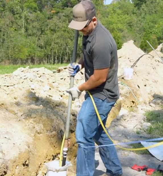 Technician installing submersible well pump equipment at excavated well site in Northern California
